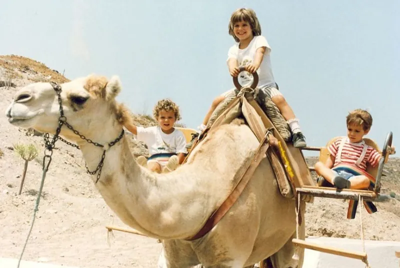 Three children riding a dromedary at Camel Park in the south of Tenerife