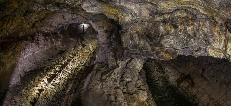 Illuminated lava tunnel in the Cueva del Viento, with a person silhouetted at the end