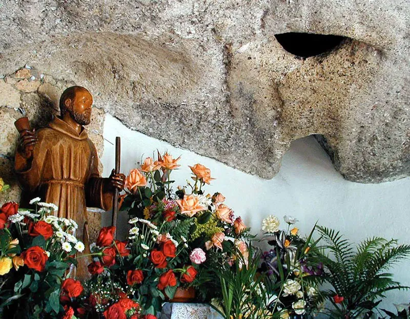 Wooden statue of the saint among roses and flowers in the rock, Cueva del Hermano Pedro