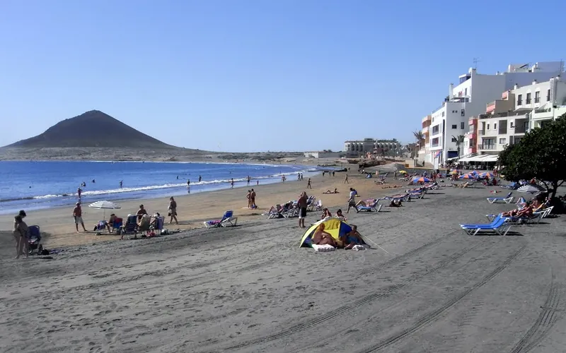 The beach at El Médano with bathers, sunbeds, white houses and Montaña Roja in the background
