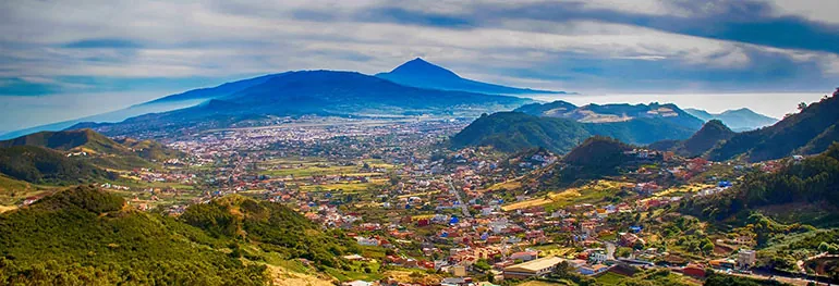Panorama of a green valley dotted with houses, with Mount Teide on the horizon, Tenerife