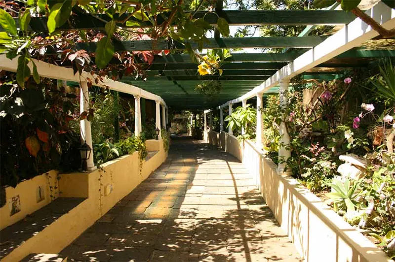 Pergola with white columns and climbing plants along a path in the Jardín Sitio Litre