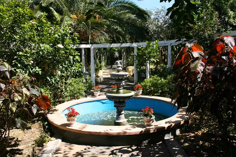 Circular fountain among palms, potted geraniums and a white pergola in the Jardín Sitio Litre