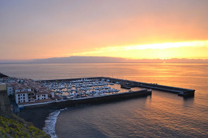 Los Gigantes marina at sunset, with moored boats and La Gomera on the horizon