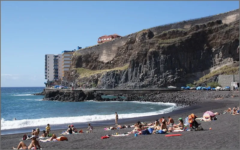 Bathers on the black sand of Playa de la Arena, Mesa del Mar, beneath the cliff