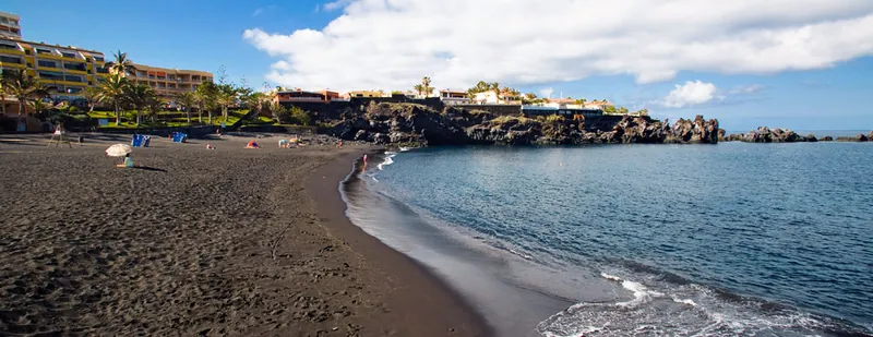 Black sand and clear water at Playa de la Arena, with palms, buildings and lava rocks