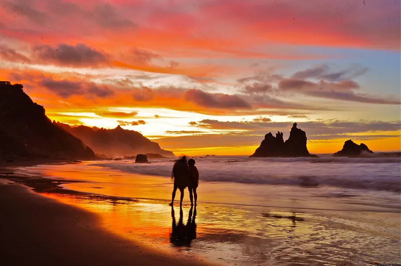 A couple silhouetted on the shoreline of Playa Benijo under a fiery sunset sky
