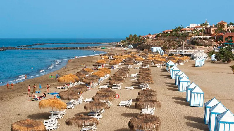 Straw parasols and white beach huts on the golden sand of Playa del Duque, Costa Adeje