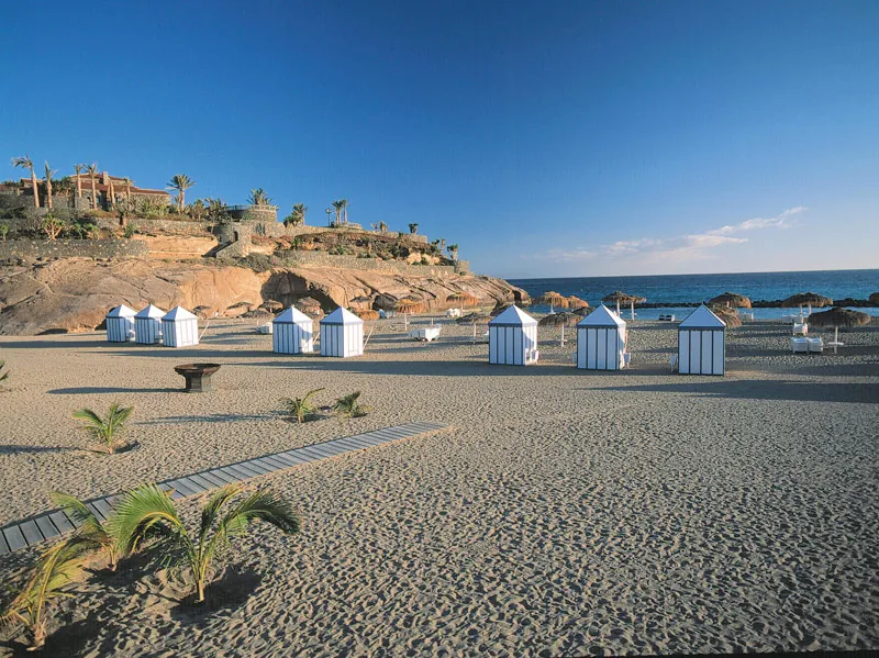 Blue-and-white striped beach huts and a wooden walkway on the sand at Playa del Duque