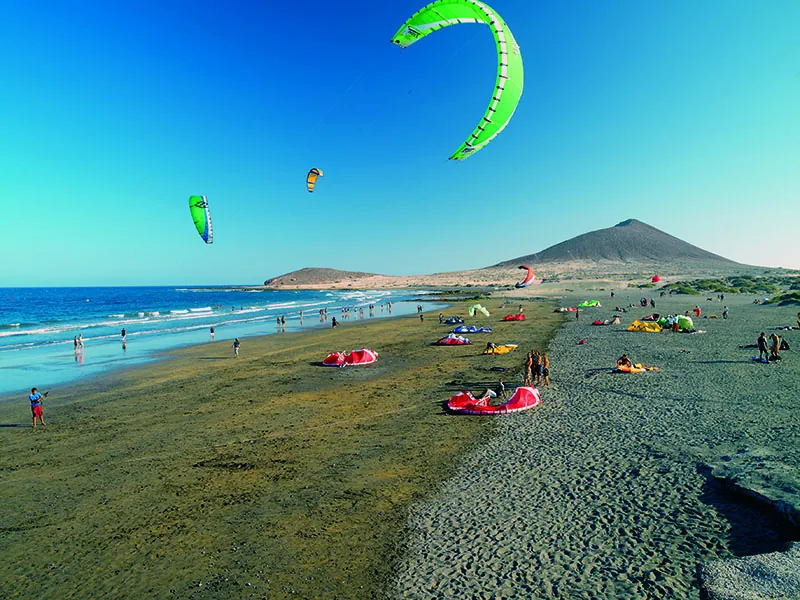 Kitesurfing kites flying over Playa El Médano, with Montaña Roja in the background