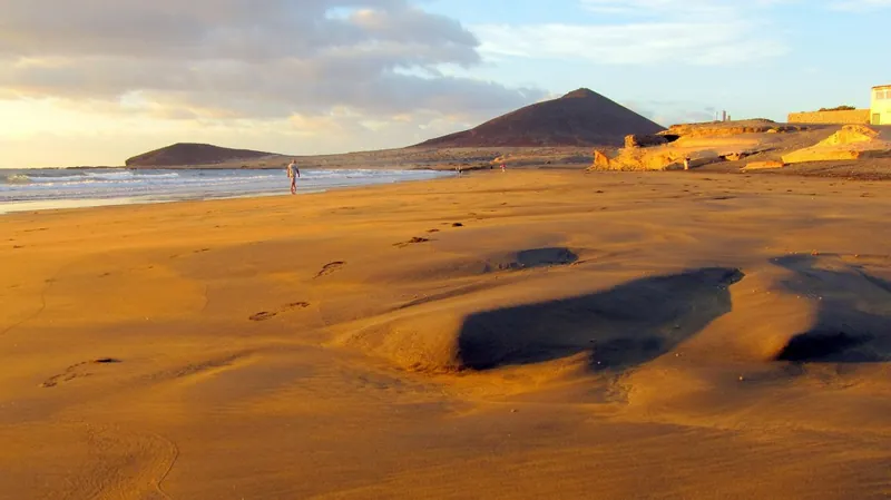 Footprints in the golden sand of Playa El Médano, with Montaña Roja in the background
