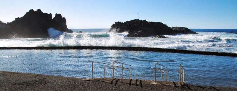 Waves breaking on the rocks beyond the natural pool with ladders and handrails, Playa El Pris