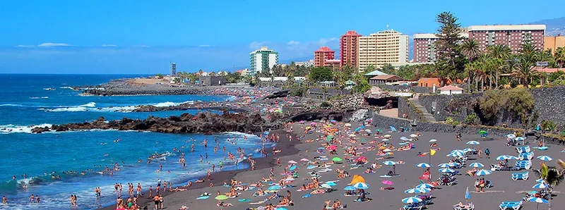 Playa Jardín crowded with bathers and colourful parasols, backed by Puerto de la Cruz’s hotels