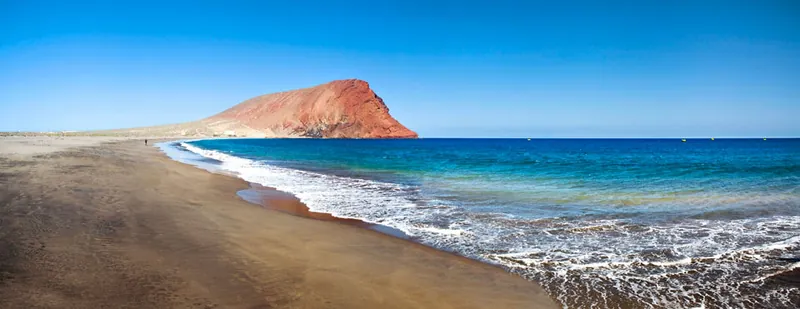 The long beach of La Tejita with waves and Montaña Roja at the far end