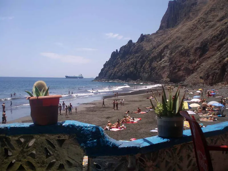 Bathers on Playa Las Gaviotas seen from a low blue wall with potted cacti and aloes