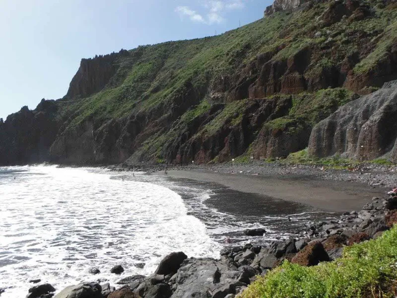 White surf on the black sand of Playa Las Gaviotas beneath steep green cliffs