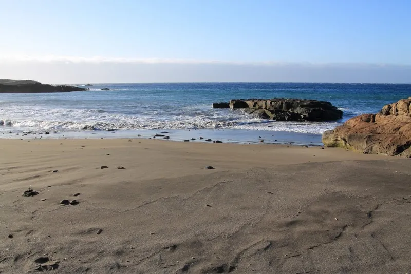 Brown sand, rocks and waves at Playa Los Abriguitos, on the coast of Abades