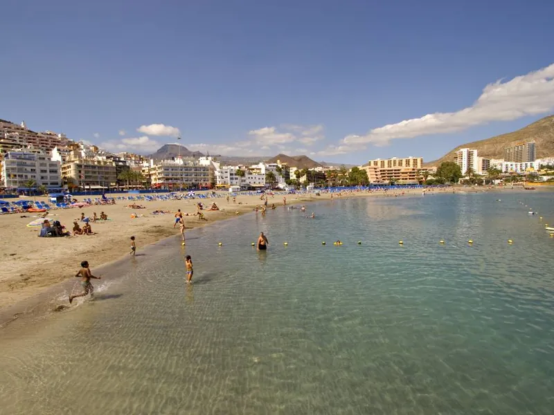 Calm, clear water at Playa Los Cristianos, with bathers, golden sand and buildings