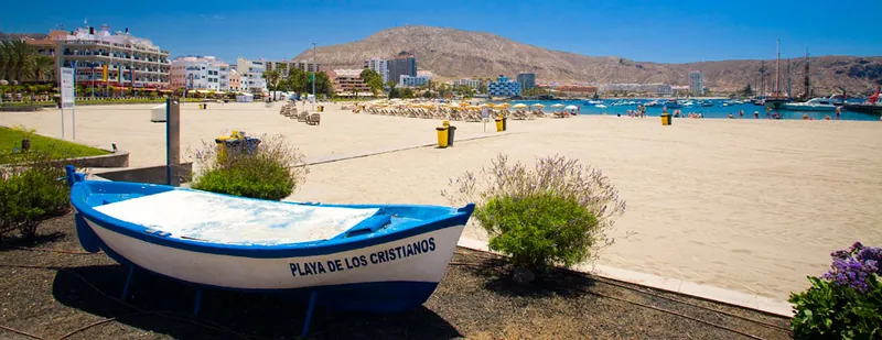 A decorative boat inscribed Playa de Los Cristianos on the seafront, with the beach behind
