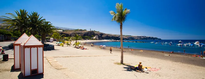 Orange-striped beach huts, palms and bathers on the golden sand of Playa San Juan
