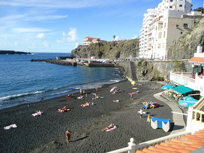 Bathers on the black sand of Playa San Marcos, with clifftop buildings and the pier