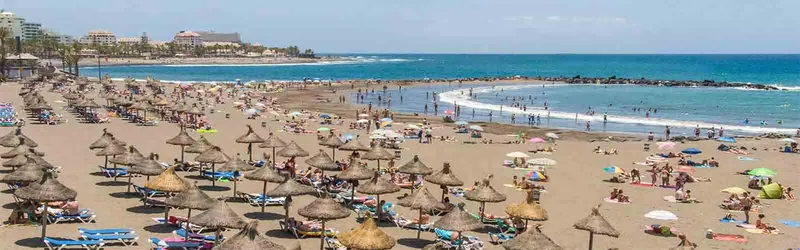 Panoramic view of Playa de Troya with rows of straw parasols, bathers and hotels