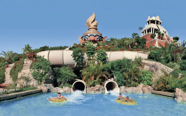 Bathers on rubber rings exit the slides among palms and Thai architecture at Siam Park